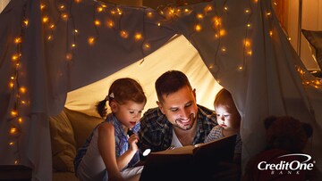 Father having fun by reading to his two kids while camping